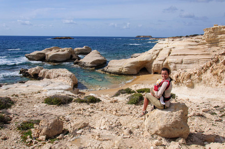 带着孩子坐在石头悬崖上看着地中海上的暴风雨的年轻女子