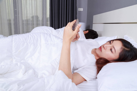 她的丈夫在睡觉的时候, 女人在床上用手机。