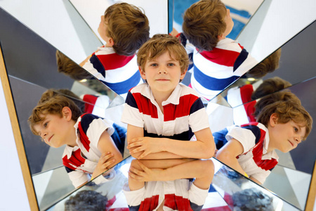 小男孩在一个博物馆的镜子的实验乐趣。快乐的微笑的学校孩子的画像