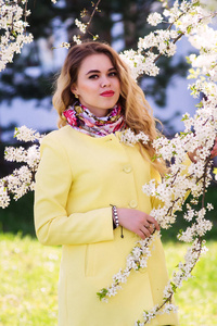 一个穿着时髦黄色大衣的年轻女子在开花的公园里。站在白色的圆圈里