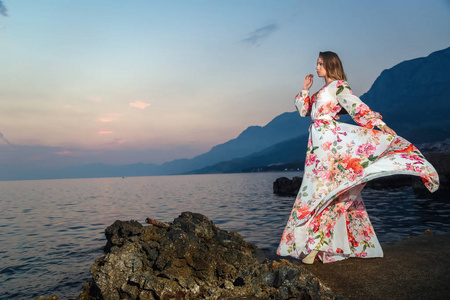 美丽的女人在夏天礼服看蓝色海和火热的日落