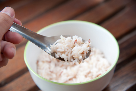 在白色圆碗和勺子木材图案背景上的白色和棕色蒸的米饭