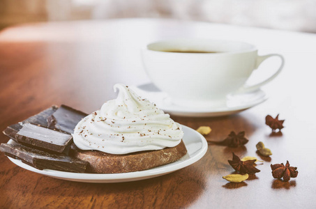 一个蛋糕, 鸡蛋白色奶油, 一块巧克力, 茴香, 豆蔻和一杯热咖啡在一个木桌上