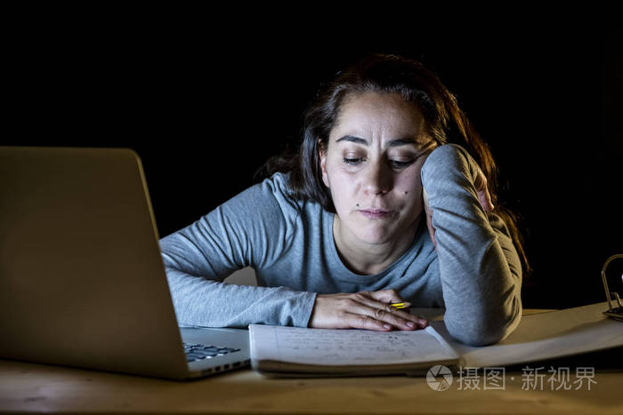 劳累和疲倦的女学生晚上工作在笔记本电脑试图不入睡