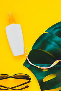 热带丛林棕榈龟背竹叶子, 太阳镜, 防晒霜空白瓶样机和妇女的泳装顶部在明亮的黄色纸背景。暑期创意平面布局概念模板文本