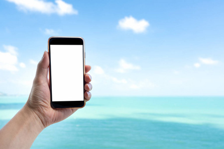 关闭男子手手持黑色智能手机在美丽的平静的蓝色海和白色的天空背景。男性手用空白白屏手机在户外暑假拍照