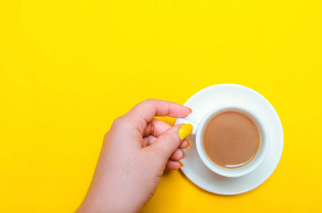一杯咖啡, 有碟和女手, 黄色的指甲在黄色的背景。极 简 主义。文本的位置。复制空间。顶部视图。平躺