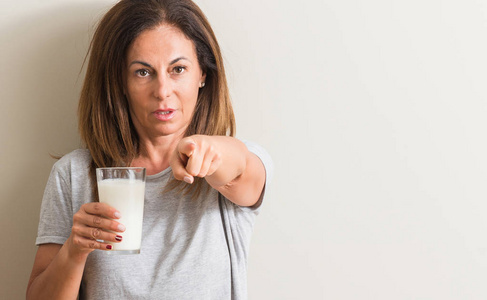 中年妇女喝一杯新鲜的牛奶指向相机和你, 手势, 正面和自信的手势从前面