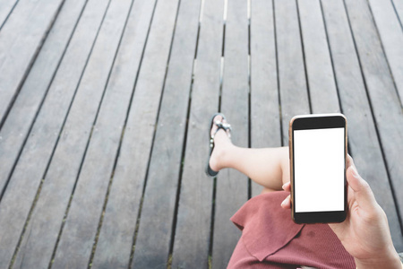 在户外木质露台背景下用空白白色桌面屏幕手持黑色智能手机的女性手的样机图像