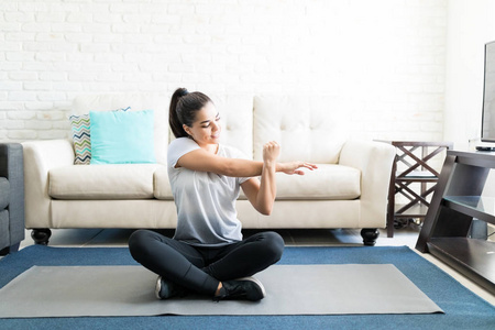 拉美裔妇女在起居室的瑜伽垫上伸展双手