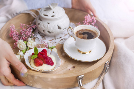 一个女人在床上喝咖啡。一个有早餐的木托盘。覆盆子浆果和花朵。浅色。浪漫。早上好