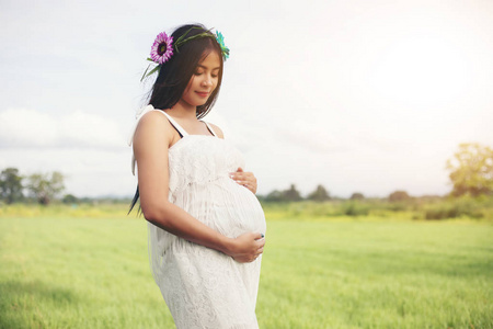 快乐和自豪怀孕的亚洲妇女看着她的肚子在公园里的日出