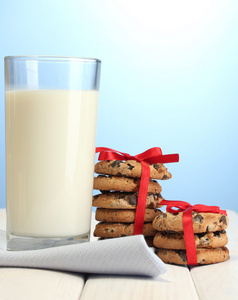 牛奶和巧克力的玻璃芯片红丝带 cookie 在蓝色背景上的木桌上