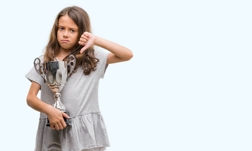 黑发西班牙裔女孩拿着一个奖杯与愤怒的脸, 否定的标志显示不喜欢拇指下来, 拒绝概念