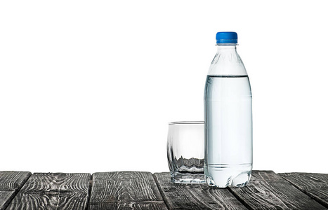 空的玻璃杯和一瓶水。塑料瓶放在木桌上。在白色背景上被隔离