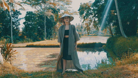 美丽的时尚女孩和服和传统的巴厘岛草帽摆在热带稻田梯田。时尚时髦女性户外肖像