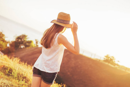戴着帽子的女孩看日落。温暖的夏日傍晚
