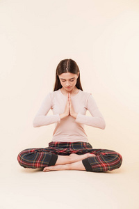 耐心的年轻的黑发女孩坐在瑜伽位置与腿交叉孤立的粉红色背景