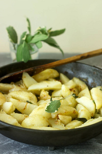 在一张混凝土桌上煎锅里放着洋葱和圣人的小土豆。选择性聚焦