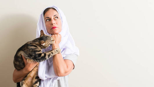 戴着白头巾的阿拉伯女人抱着一只猫严肃的脸思考问题, 非常困惑的想法