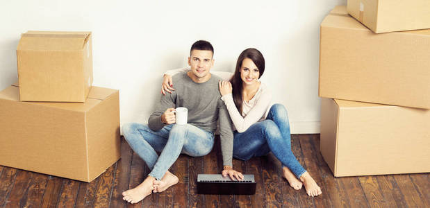 男人和女人用笔记本电脑和一个盒子。年轻夫妇用手提电脑浏览互联网。在一个新的家庭概念中移动