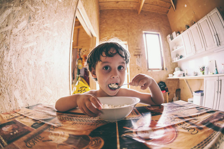 这个男孩吃了一个小干酪勺, 坐在一个宽敞的饭厅里的桌子上。