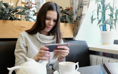 在她的手机上的咖啡馆里, 年轻的女人黑发的茶壶和茶杯的照片。前视图