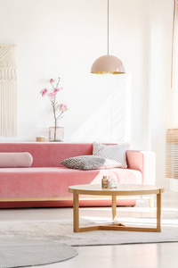 复古风格, 千禧粉色吊灯上方一个简单的, 木制的茶几在一个阳光明媚的, 白色的客厅内部与图案枕头在天鹅绒沙发上
