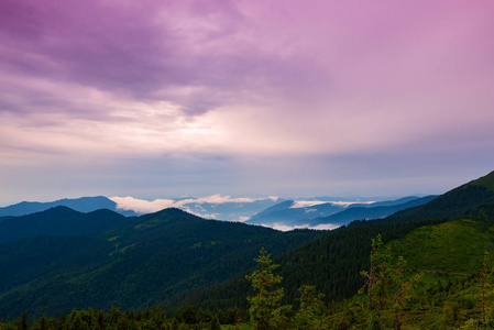 壮观的山风景在风暴之前, 重的灰色云彩漂浮在绿色树木繁茂的山之上到地平线在日落期间。广角