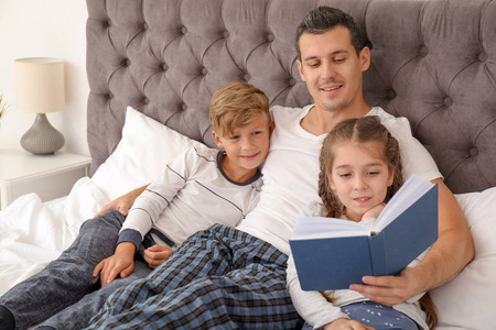 父亲在卧室里看书和孩子们在一起。幸福家庭