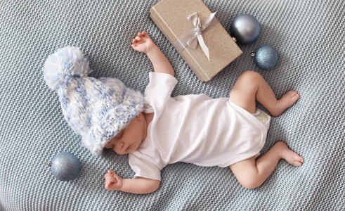 可爱的婴儿在针织帽子与圣诞节装饰和礼品盒睡在毯子上
