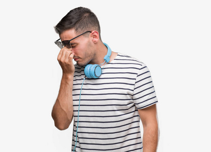 英俊的年轻人戴着耳机疲倦的揉鼻子和眼睛感到疲倦和头疼。压力和挫折概念