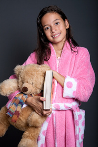 年轻女孩准备睡觉与书和泰迪在手臂