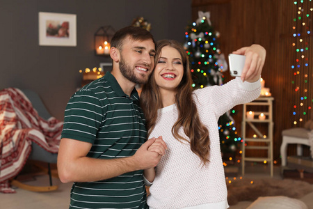 愉快的年轻夫妇采取自拍在装饰为圣诞节房间