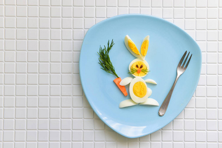 孩子们的快乐早餐。兔子从鸡蛋和胡萝卜。躺在蓝色的盘子上