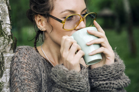 穿着毛衣戴眼镜的年轻女子在公园里喝咖啡的画像