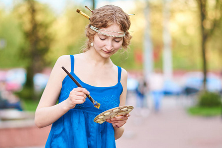 美丽的女孩艺术家在街上的蓝色礼服, 微笑着, 在她手中的流苏和调色板