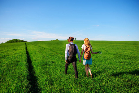 有了背包, 戴着帽子的男人和长头发的女人沿着小路走。一对夫妇沿着草地散步