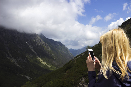 一个穿着蓝色夹克的年轻金发女郎在峡谷的背景下站在山上。概念。旅游, 旅游, 徒步旅行