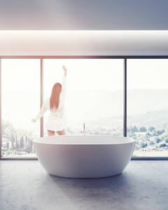 妇女在浴室内部与混凝土地板, 一个全景窗口, 山景和白色优雅的浴缸。3d 渲染色调图像