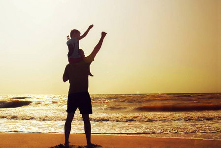 父亲和儿子在日落的时候在海滩上玩。友好的家庭的概念