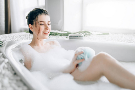 使用海绵在浴缸中的年轻妇女泡沫, 放松和水疗