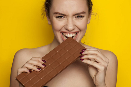 快乐的年轻女人喜欢吃巧克力的黄色背景