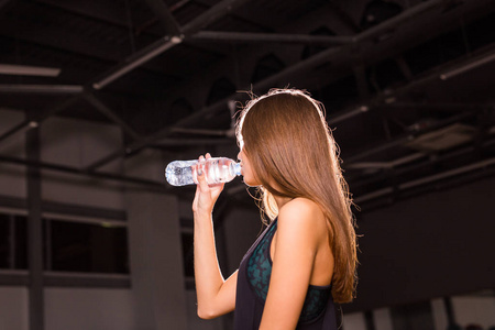 健身女人喝水从瓶子里。在健身房休息从锻炼肌肉年轻女性