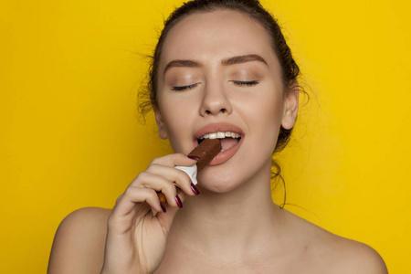 快乐的年轻女人喜欢吃巧克力的黄色背景