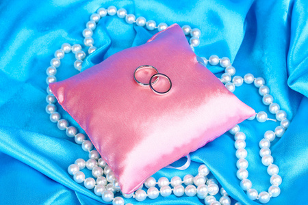 蓝色布料背景上的缎面枕上的结婚戒指