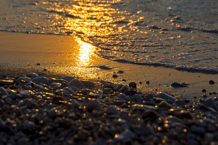 在日落的灯光下, 在鹅卵石海滩特写镜头与冲浪海。在傍晚的日落中, 不同大小的石头在大海的背景上。浅景深和美丽的波克