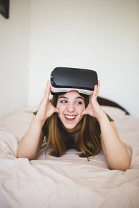 美丽的十几岁的女孩与虚拟现实护目镜躺在床上, 准备玩视频游戏