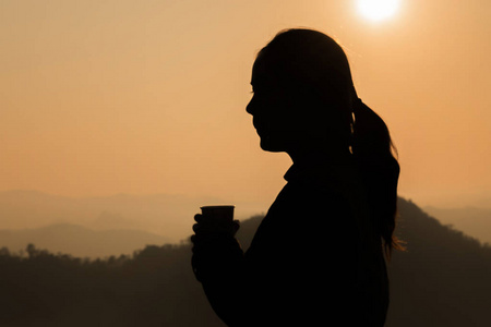 妇女的黑暗的剪影拿着杯子茶在橙色背景与山
