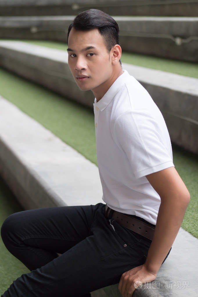 的男人坐在城市环境中;具有棕褐色皮肤和短发的年轻成人东南亚人模型